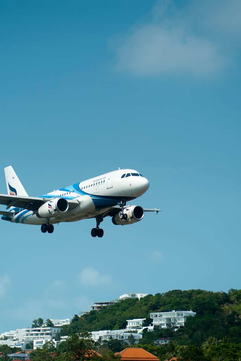 A passenger airplane descends for landing over lush hills in sunny Thailand.